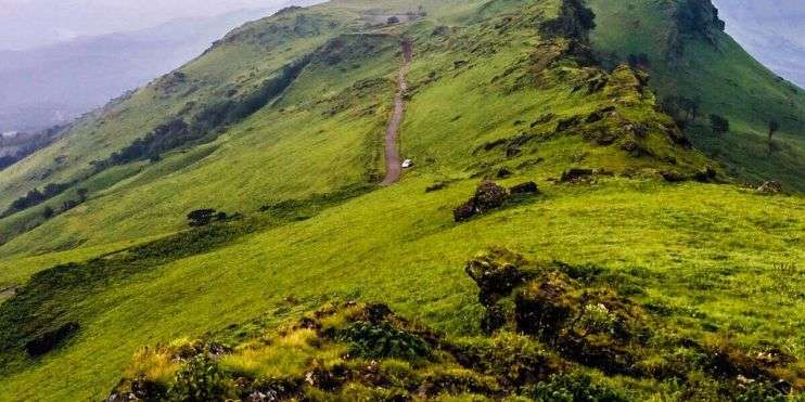 A scenic road winding through the lush green Baba Budangiri mountain range, a sacred site with ancient caves and trekking trails.