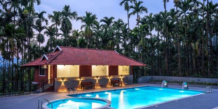 A serene pool reflecting the fading light of dusk, encircled by tall palm trees, creating a tranquil ambiance.