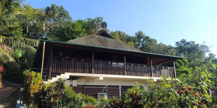 A house with a balcony and a roof on top of a hill, nestled amidst the verdant landscapes near Kalhatti Falls.