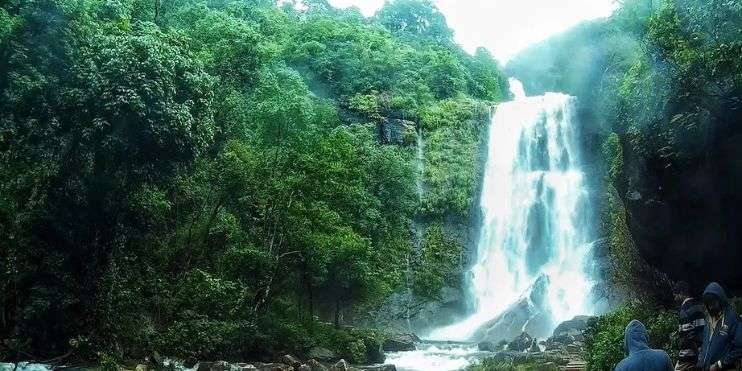 A group of people standing near Hebbe Falls, a picturesque waterfall with two stages, Dodda Hebbe and Chikka Hebbe.