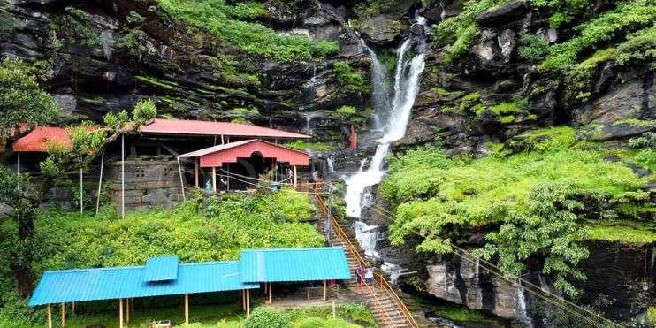 A serene waterfall cascades near a quaint house nestled in nature.