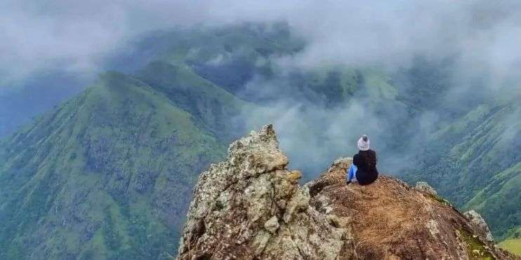A person sitting on a mountain peak, gazing at the valley below, surrounded by breathtaking scenery.