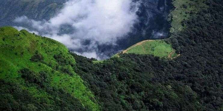 Aerial view of majestic mountains with fluffy clouds floating above.