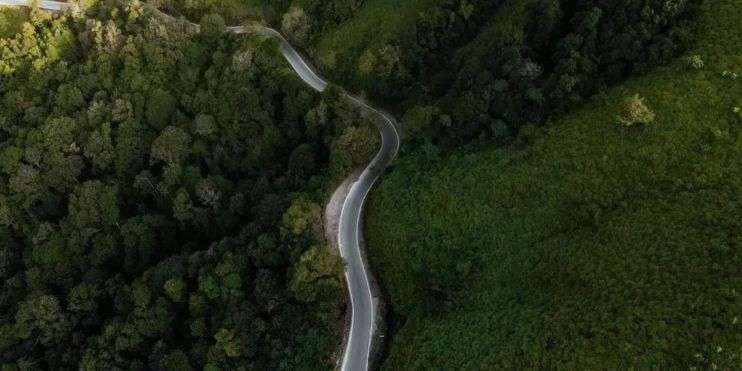 Aerial view of a winding mountain road cutting through lush green forests and rocky terrain.