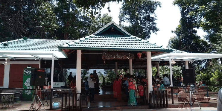 People standing outside restaurant in park, enjoying the outdoor seating and beautiful surroundings.