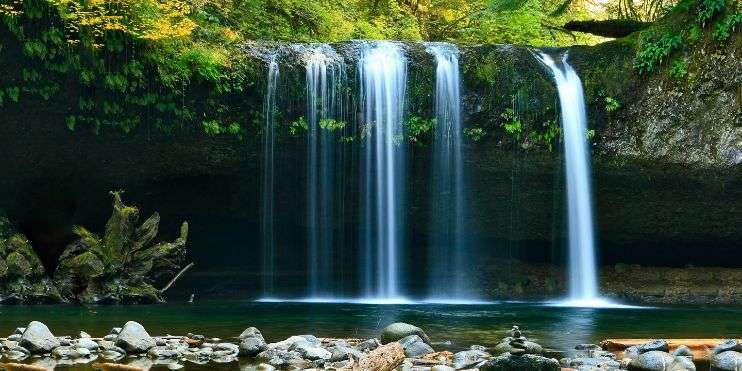 A high-definition wallpaper featuring a stunning waterfall cascading down rocks surrounded by lush greenery.