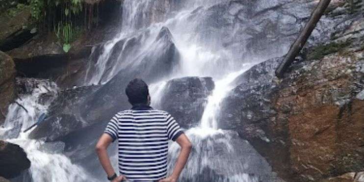 A man standing in front of a majestic waterfall, surrounded by lush greenery and misty air.