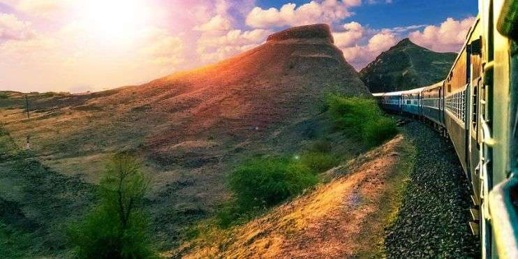 A train winding through mountainous terrain as the sun sets, casting a warm glow over the landscape.