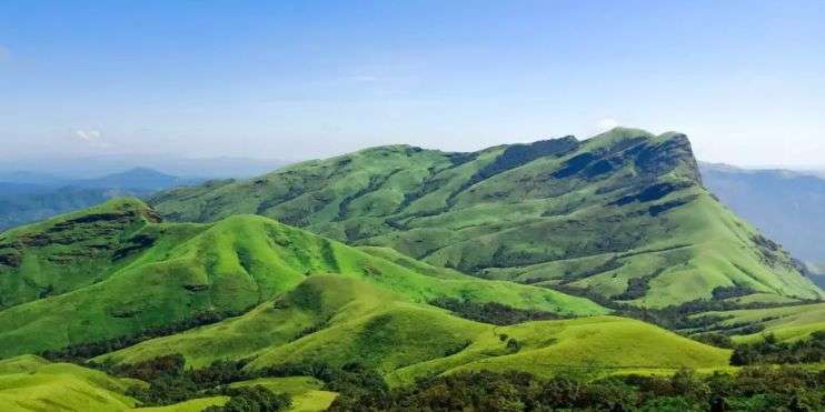 Rolling green hills of Kerala, India, under a clear blue sky.