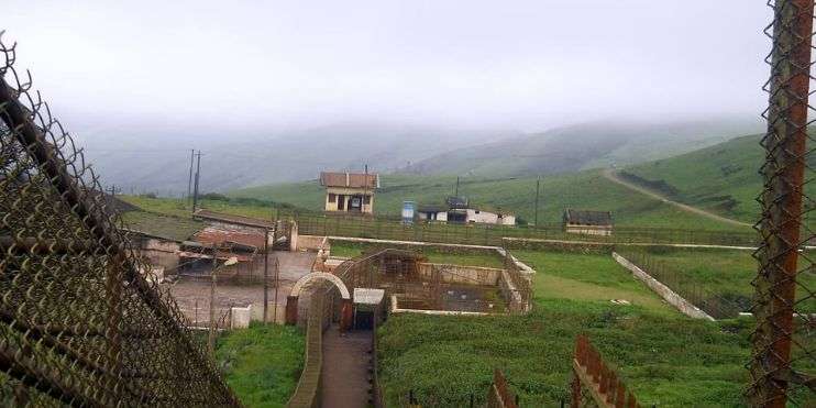 A scenic hillside with a fence, building, and Baba Budangiri pilgrimage site in the background.