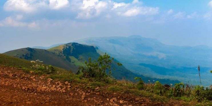 A dirt road leading to Baba Budangiri mountain range in the Western Ghats, with a blue sky.