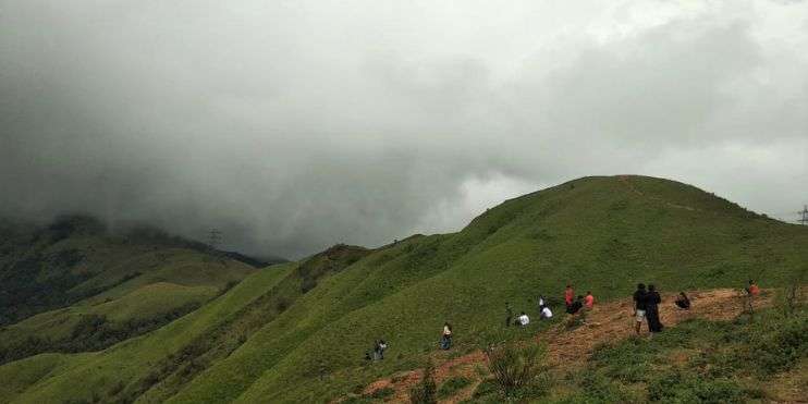 Hikers ascending a hill under cloudy skies. Best Time to Visit Devaramane.