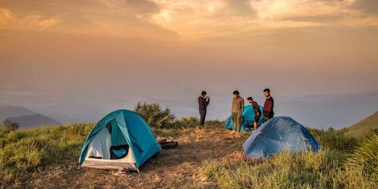 Four people standing near tents on a hillside at Bandaje Falls campsite, surrounded by nature's tranquility.