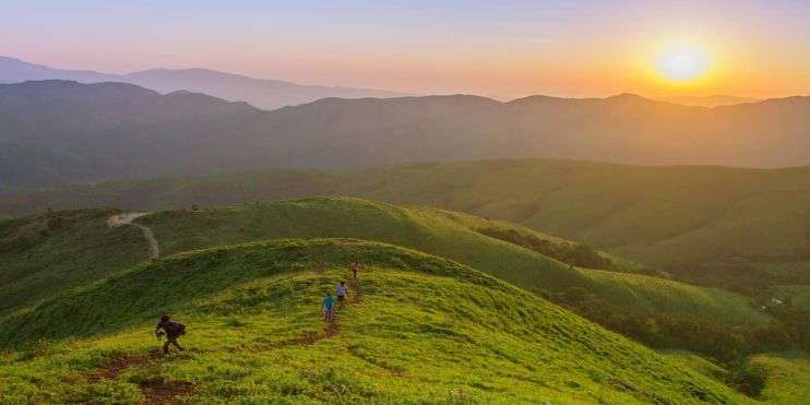 A group of hikers trekking up a mountain trail as the sun sets in the background, casting a warm glow over the landscape.