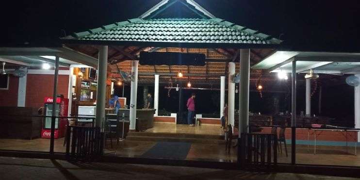 People standing outside a restaurant at night, with the sign "Return to Bynekaadu Resort, Enjoy Sunset and Local Dinner