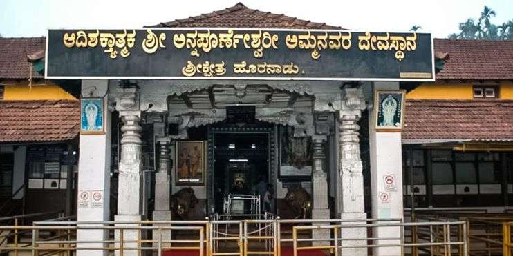 Entrance to Indian temple with intricate carvings and colorful decorations, surrounded by lush greenery.