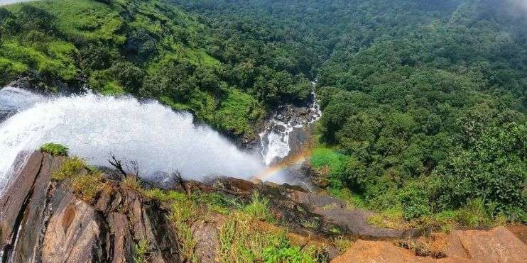 Aerial view of a waterfall in a forest. How to Reach Bandaje Falls: Trek through the lush greenery to witness this natural beauty.