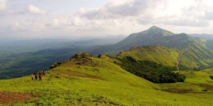 People trekking on lush green hills of Mullayanagiri, Karnataka, enjoying panoramic views of Western Ghats.