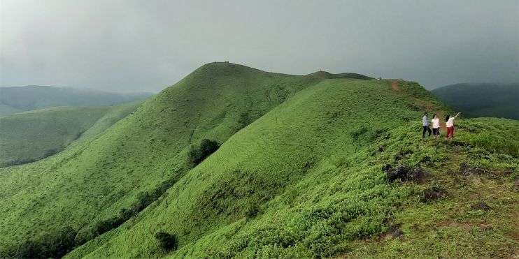 Two people standing on top of a green mountain, enjoying the scenic view.