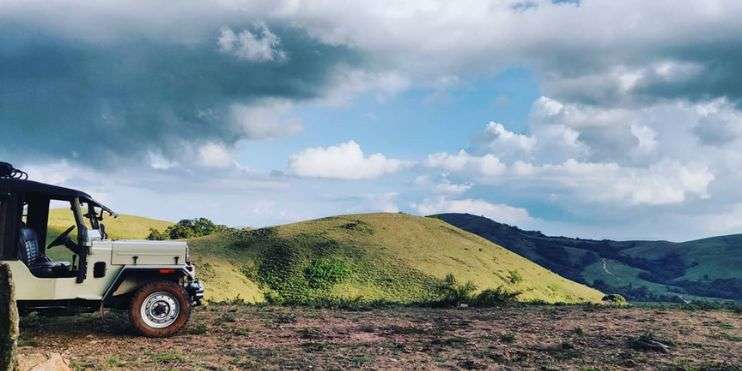 A jeep parked on a hilltop with fluffy clouds in the background.