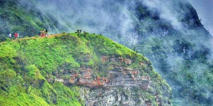 People walking on steep mountain trail with green grass, heading to Ballalarayana Durga Fort.