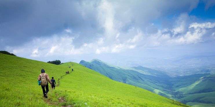 Two hikers ascending a mountain in lush valley, surrounded by greenery and clear skies.