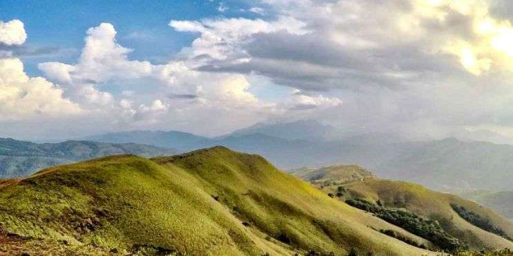 A scenic view of mountains from a hill, with lush greenery in the foreground and a clear blue sky above.