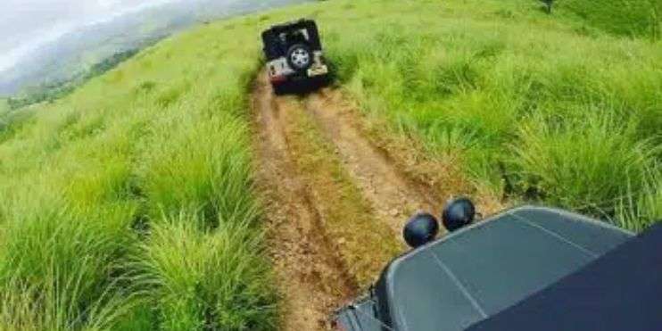 A jeep navigates a grassy hill, showcasing the thrill of off-road adventures in the scenic Western Ghats of Chikmagalur.