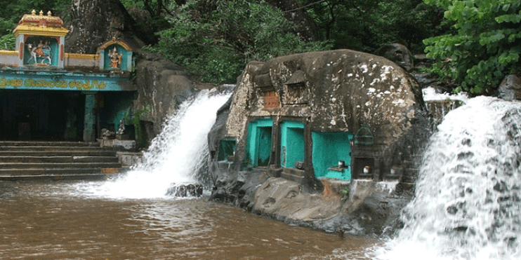 A serene waterfall cascades in front of a temple, showcasing the natural beauty of Kallathigiri Falls near Kalasa.