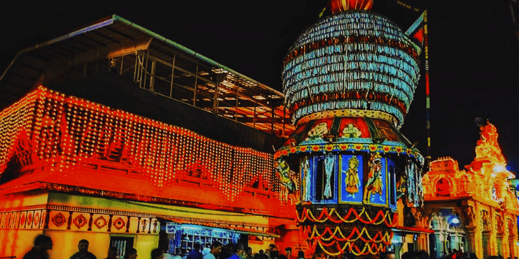 A large, brightly lit building adorned with festive decorations, symbolizing the vibrant Puttige Utsava festival in Udupi.