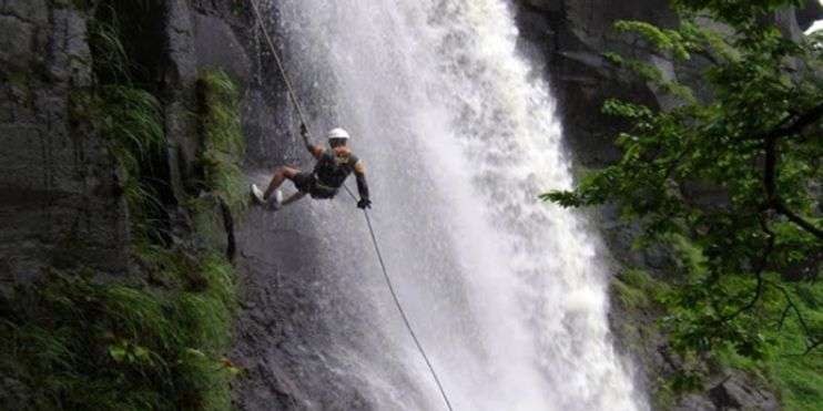  A man on a rope hangs from a waterfall, highlighting the adventurous spirit of rock climbing in the stunning Western Ghats.