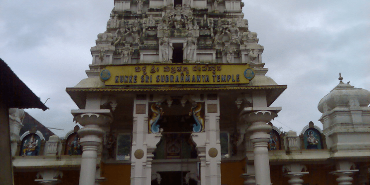 Subramanya Temple, a large white structure, prominently displays a significant sign, surrounded by greenery.