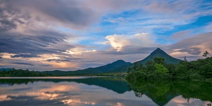  A serene lake reflects a majestic mountain range, surrounded by lush greenery and tranquil colonial architecture.