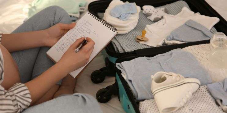  A woman sits on a bed with a suitcase, writing in a notebook, preparing for her Kurinjal Peak trek essentials.