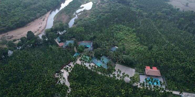 Aerial view of a serene resort by a river, showcasing the tranquil landscape of Karnataka and its lush surroundings.