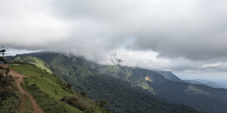 A dirt road ascends towards a mountain, framed by clouds, inviting travelers to the scenic Maidaadi Sunset Viewpoint.