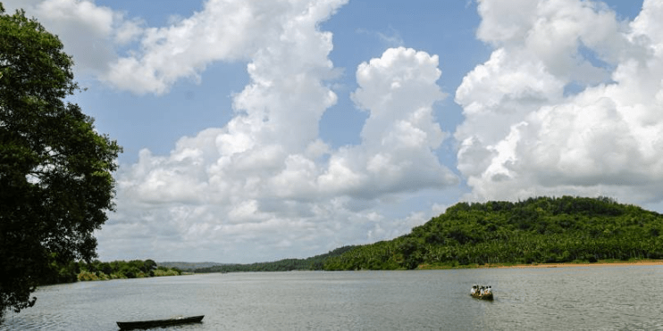 A boat glides on the river, framed by a hill, showcasing the serene beauty of the Netravathi River's landscape.