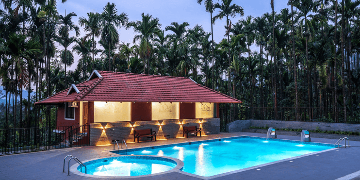 A tranquil pool surrounded by palm trees at dusk, reflecting the serene beauty of nature at Bynekaadu Resort.