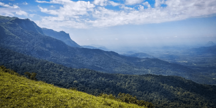 A breathtaking panoramic view from a mountain in Sri Lanka, showcasing rolling hills and distant mountain ranges at sunset.