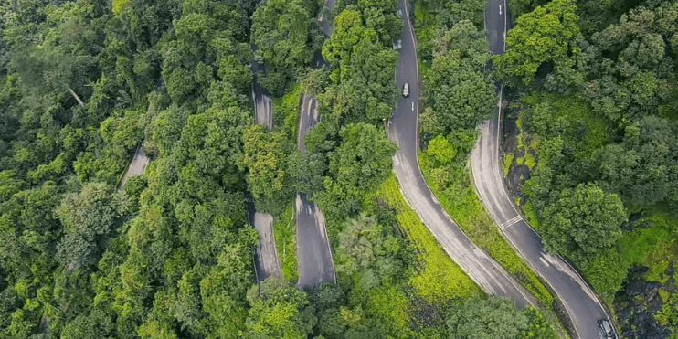 Aerial view of a winding road through a lush forest, showcasing the beauty of nature and the tranquility of the Agumbe region.