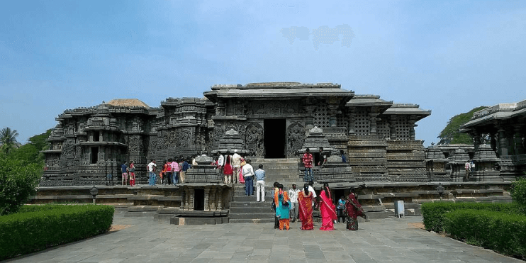 People standing outside an ancient Hoysala temple, showcasing intricate sculptures and spiritual significance in Karnataka.