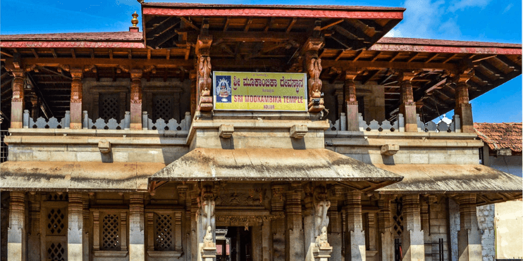 A large building with a prominent sign, set against the serene backdrop of the Western Ghats in Karnataka.