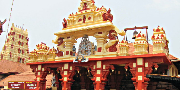 A large building featuring a prominent red and white tower, representing the Udupi Sri Krishna Temple in Karnataka.