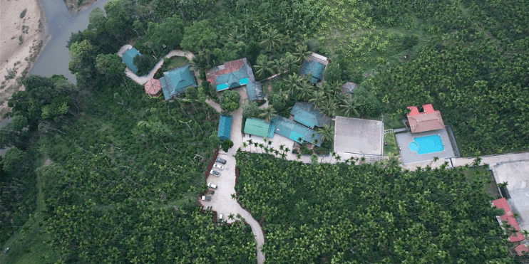 Aerial view of Bynekaadu Resort in Chikmagalur, surrounded by lush greenery and a winding river, showcasing nature's beauty.