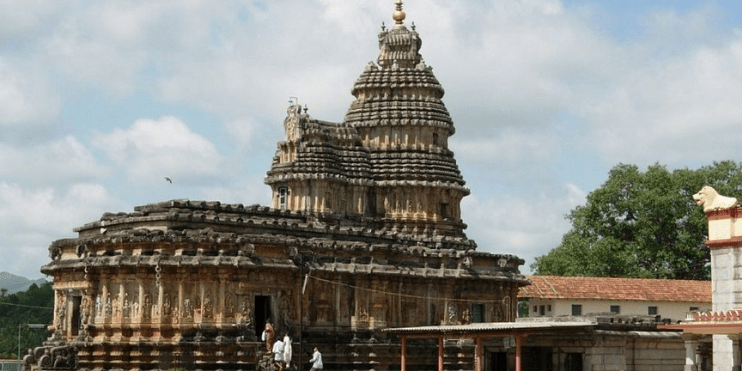 A large temple with an impressive central tower, surrounded by serene gardens and a tranquil river, reflecting spiritual history.