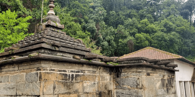 A stone building with a roof and wall, part of the historic Ballalarayana Durga Fort, surrounded by natural beauty.