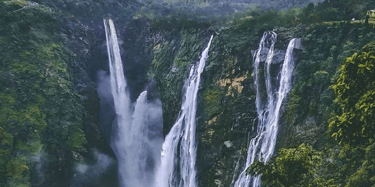 A large waterfall cascades through a lush forest, surrounded by greenery and attracting visitors for its beauty and spirituality.