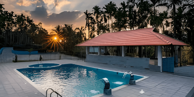 A serene pool with a red roof, framed by lush greenery, as the sun sets behind the tranquil landscape of Chikmagalur.