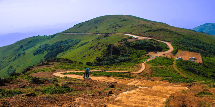 A man walks along a mountain path, enjoying the stunning views from Mullayanagiri Peak in Karnataka.