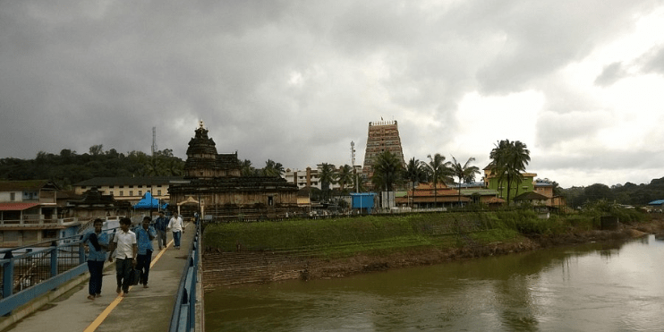 People walking across a bridge over the Tunga River, with the Vidyashankara Temple visible in the background.